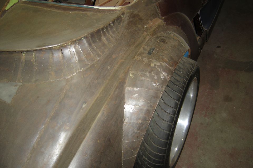 Bare metal rear fender with pie-cut welds over a wide tire on a polished deep-dish wheel, custom bodywork in progress