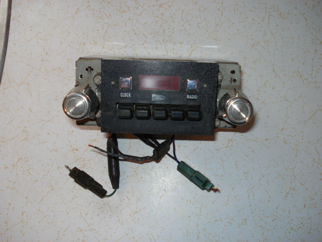 Car radio with knobs, buttons labeled CLOCK and RADIO, and a red digital display