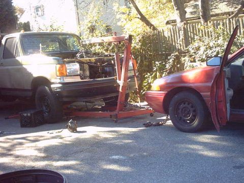 1979 Ford Bronco - Two vehicles and an engine hoist are present in an outdoor setting, possibly during maintenance.
