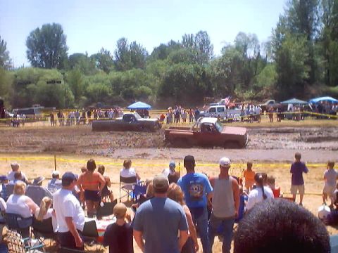 1976 Ford F-100 - Spectators watch as trucks navigate a muddy course during an event.