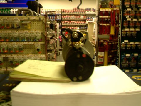 1987 Ford Bronco II - A starter motor sits on a stack of paper in front of shelves stocked with auto parts.