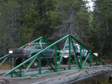 1986 Ford Bronco - Modified pickup trucks navigate a forest bridge.
