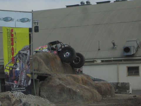 1990 Ford Bronco - tube-frame rock-crawling buggy with large knobby tires climbs a staged boulder at an outdoor UROC competition course.