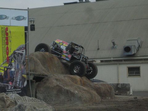 1990 Ford Bronco - tube-frame rock buggy with oversized tires balances atop a large boulder during a rock-crawling event.
