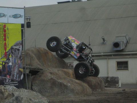 1990 Ford Bronco - rock-crawling buggy lifts its front end while flexing its suspension between two staged boulders at a UROC event.