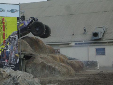 1990 Ford Bronco - purple tube-chassis rock buggy lifts its front wheels skyward as it attacks a large boulder at a rock-crawling event.