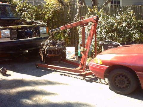 1979 Ford Bronco - An engine is being removed from a vehicle using an engine hoist, with a red car visible in the foreground.