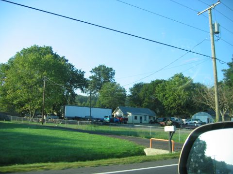1971 Ford Ranchero - A rural property features a house, a long trailer, and multiple vehicles parked in the yard under a clear blue sky.
