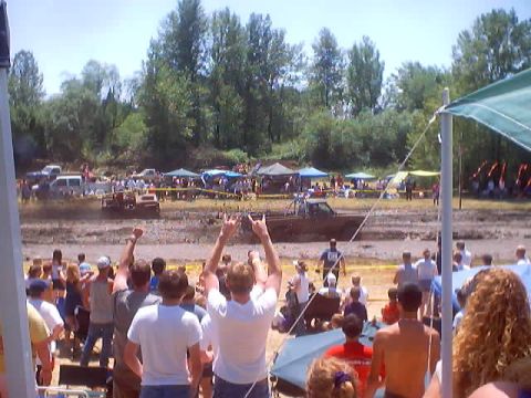 1976 Ford F-100 - Spectators watch vehicles compete in a mud bogging event with tents and trees in the background.