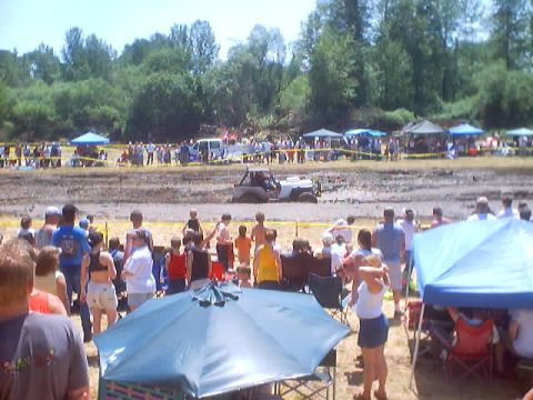 1976 Ford F-100 - Spectators gather to watch vehicles navigate a muddy course during an outdoor event.
