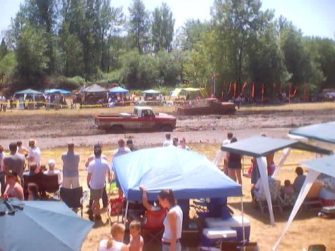 1976 Ford F-100 - A red pickup truck is stuck in the mud at an outdoor event with spectators and tents.