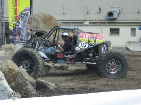 1990 Ford Bronco - black tubular-frame rock crawler buggy marked number 123 with Mickey Thompson and BFGoodrich decals climbs a man-made rock obstacle.