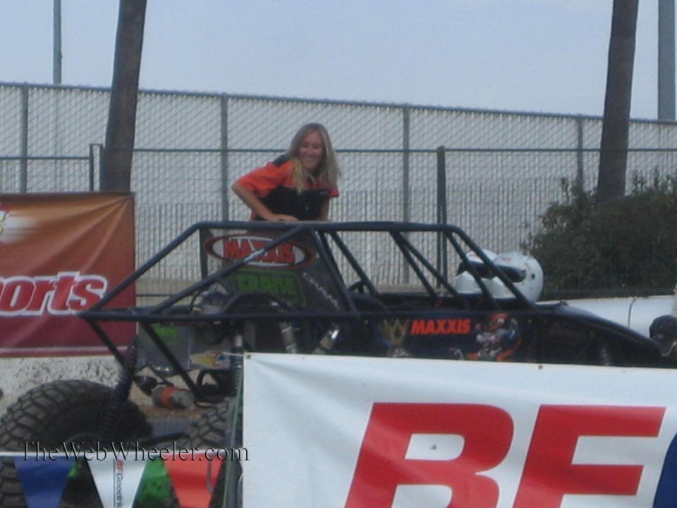 Smiling woman in orange shirt standing behind a Maxxis-sponsored tube buggy at an outdoor event