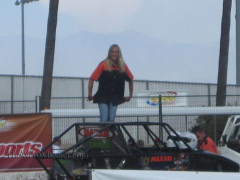 1990 Ford Bronco - blonde woman in an orange shirt stands atop the roll cage of a Maxxis-sponsored buggy with mountains and event banners behind her.