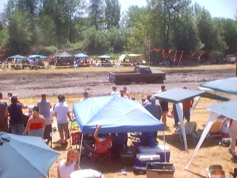 1976 Ford F-100 - A muddy field event with tents and people gathered, while a truck is stuck in the mud.