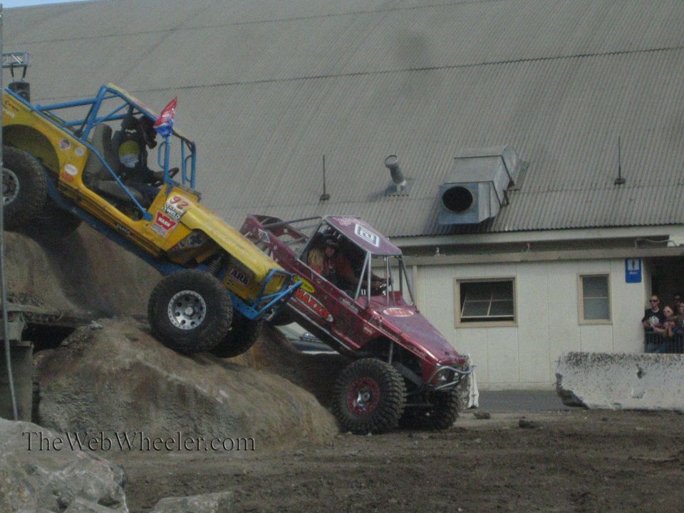 Yellow buggy and maroon buggy descending a rock obstacle with spectators watching