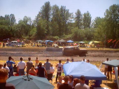 1976 Ford F-100 - A brown 1978 Ford Bronco navigates a muddy track during an event, with onlookers and tents in the background.