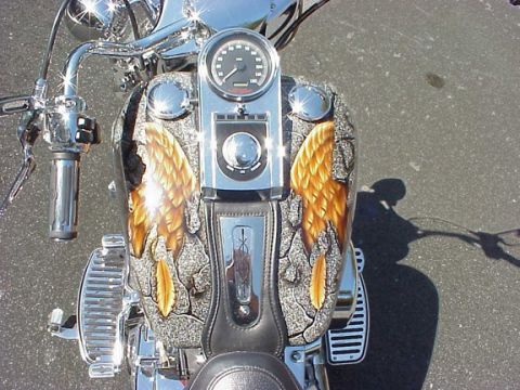 1999 Harley-Davidson Fat Boy - A motorcycle's front view showcases a custom paint job angel wings on the gas tank, complemented by shiny chrome accents.
