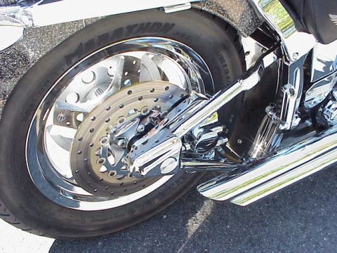 1999 Harley-Davidson Fat Boy - Close-up view of the rear wheel, brake system, and dual exhaust pipes on a motorcycle.