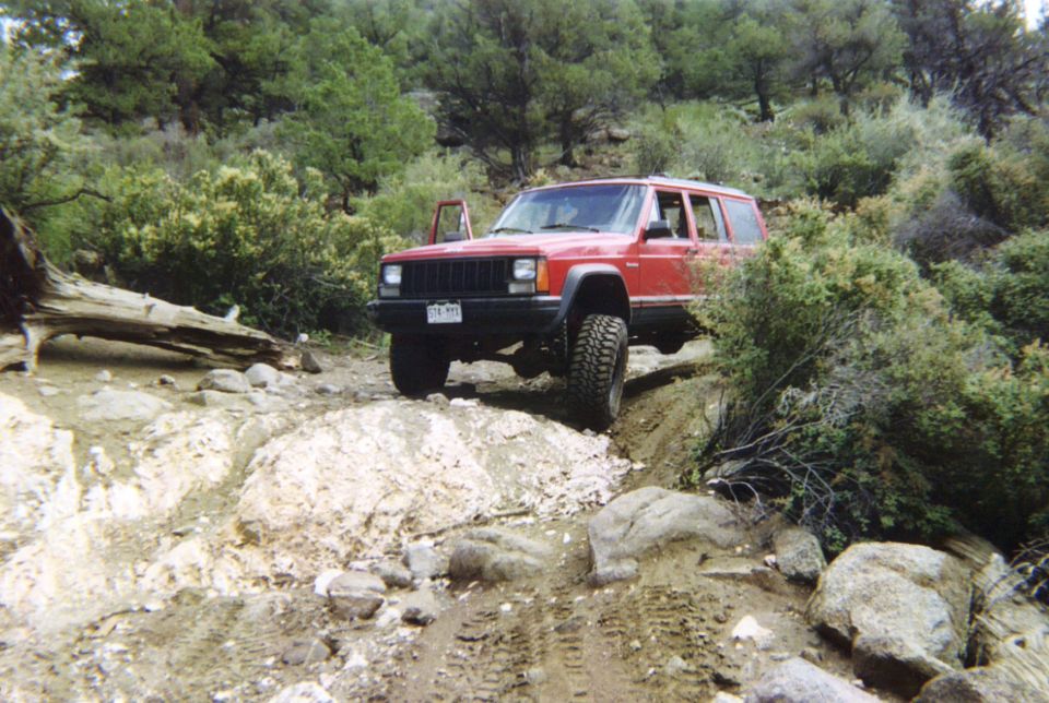 Red lifted Jeep Cherokee XJ descending a rocky rutted trail through juniper brush