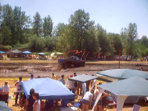 1976 Ford F-100 - A truck is stuck in a mud pit during an event, with spectators gathered under tents.