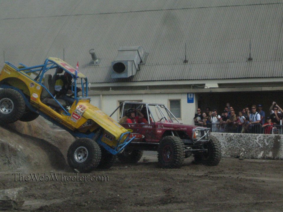 Yellow buggy climbing rock with maroon buggy alongside and spectators watching