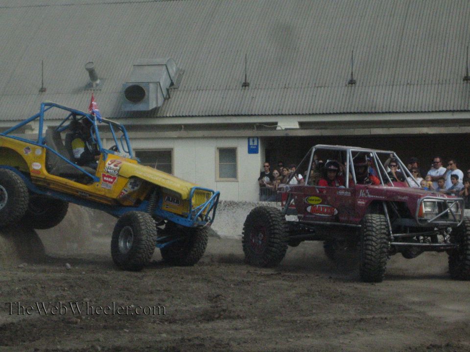 Yellow buggy and maroon buggy racing across a dirt course with spectators watching
