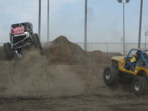 1990 Ford Bronco - maroon rock buggy kicks up heavy dust on a dirt mound while a yellow and blue buggy works the slope alongside it.