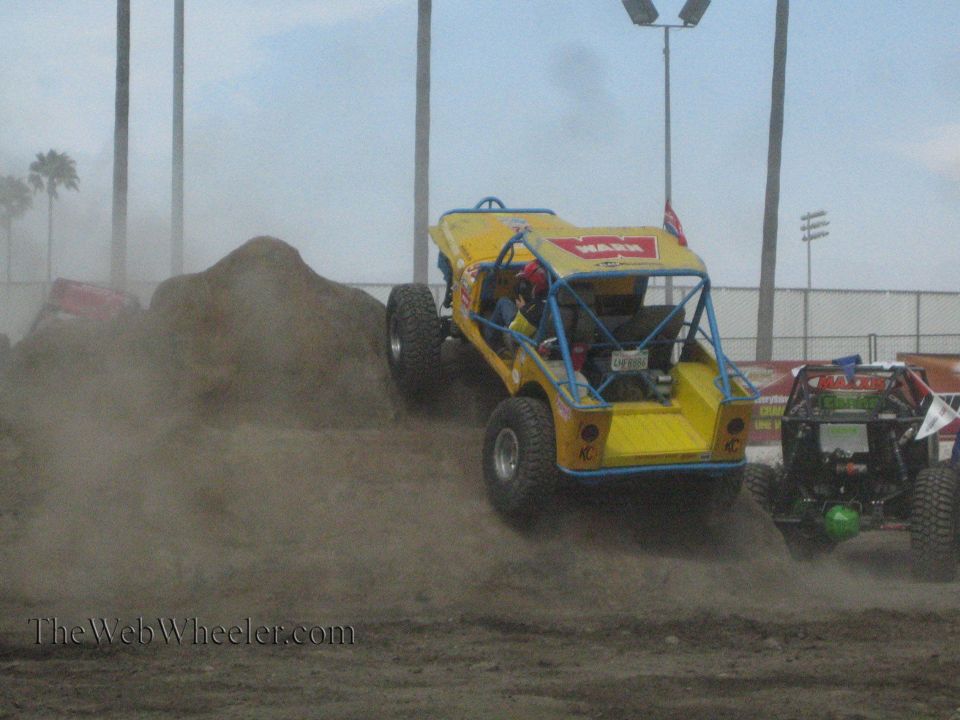 Yellow Warn buggy climbing a dirt mound throwing dust with buggies behind