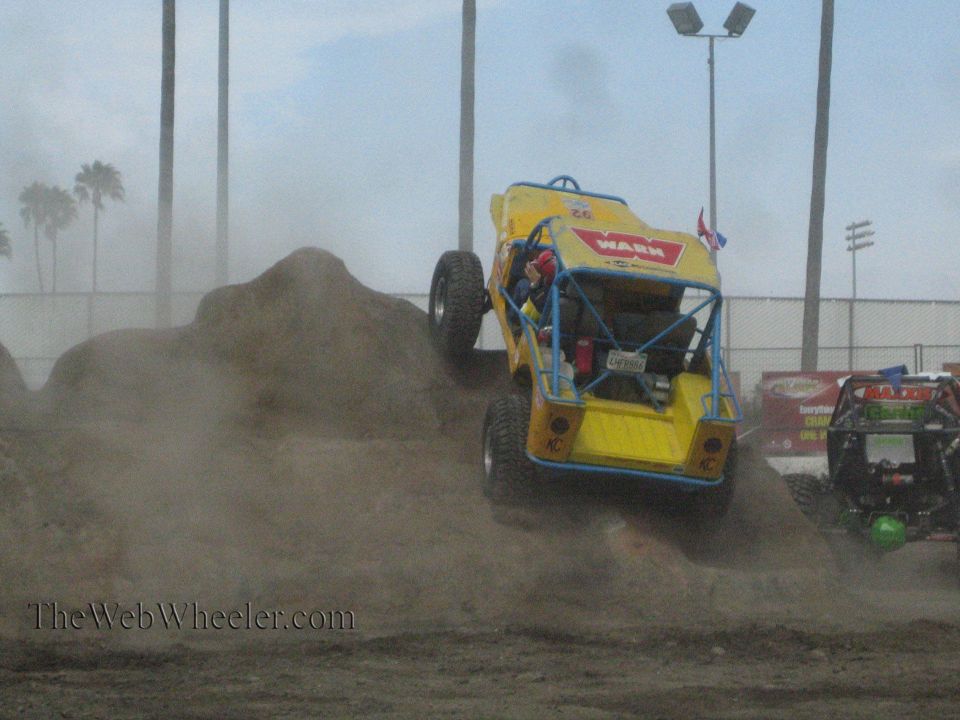 Yellow Warn buggy climbing a dirt mound in heavy dust at an outdoor course