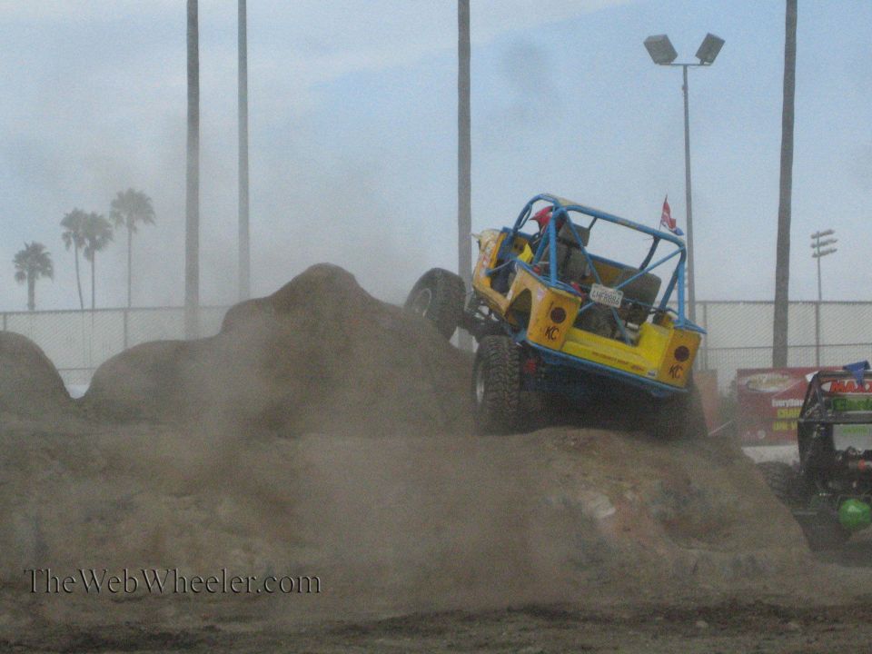 Yellow and blue rock buggy descending a dirt obstacle in a dusty arena
