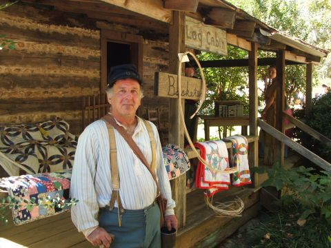 1966 Ford Ranchero - Historical reenactment scene at a log cabin a man in period attire and displayed quilts.