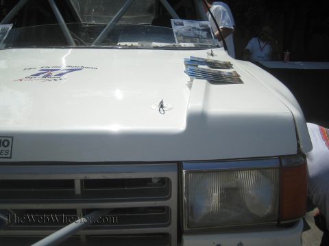 1990 Ford Bronco - Close-up of a white off-road truck's hood and grille with promotional brochures and decals laid across the hood.