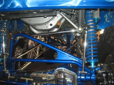 1990 Ford Bronco - Detail of a custom blue truck's underside showing tubular suspension links, blue coilover shocks and a brake rotor.