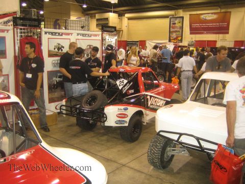 1990 Ford Bronco - Red and white off-road race trucks, including a Victory-sponsored No. 25, fill a busy TrophyKart expo booth.