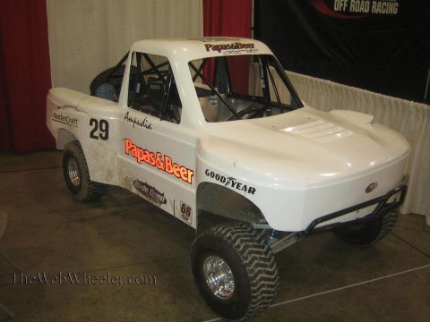 1990 Ford Bronco - white Papas and Beer No. 29 short-course off-road race truck with Goodyear decals sits on display at an indoor booth.