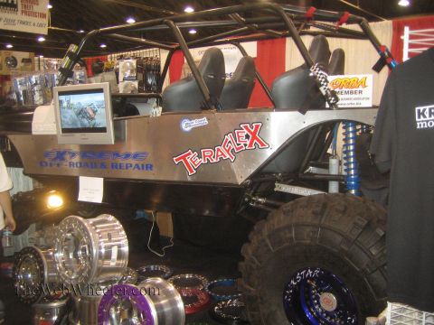 1990 Ford Bronco - open tube-frame rock buggy with Extreme Off-Road and TeraFlex graphics sits behind stacks of off-road wheels at a booth.