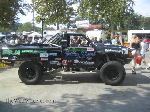 1990 Ford Bronco - black No. 706 Villa Ford / Baja Motorsports off-road race truck sits parked on pavement amid a crowd at an outdoor event.