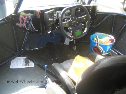 1990 Ford Bronco - Interior of a caged off-road race vehicle showing a removable round racing wheel, floor shifter, bucket seat and a devil-girl decal on the…