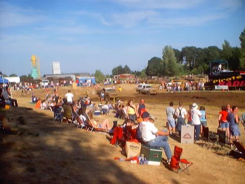 1976 Ford F-100 - Spectators watch a mud bog event with various vehicles present under a clear blue sky.
