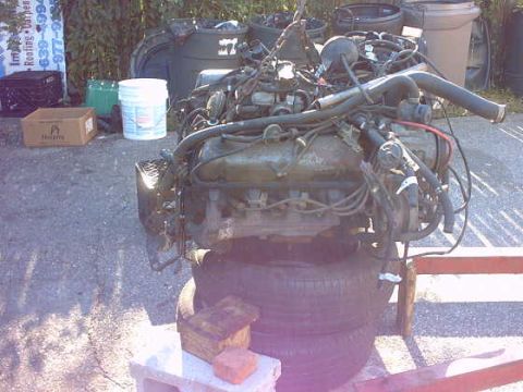 1979 Ford Bronco - Engine assembly on tires, with background of trash cans and building materials.
