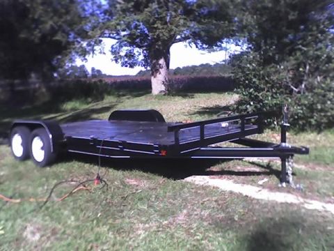 1978 Ford Bronco - A black car trailer with dual axles is parked on a grassy area with trees in the background.