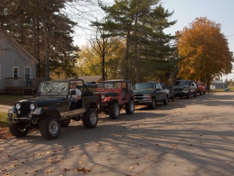 1979 Jeep CJ5 - A line of Jeeps and trucks are parked on a street during the fall season.