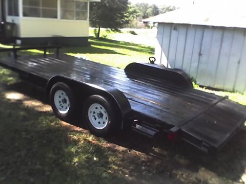 1978 Ford Bronco - A black car trailer with dual axles and white rims is parked on a grassy area next to a building.