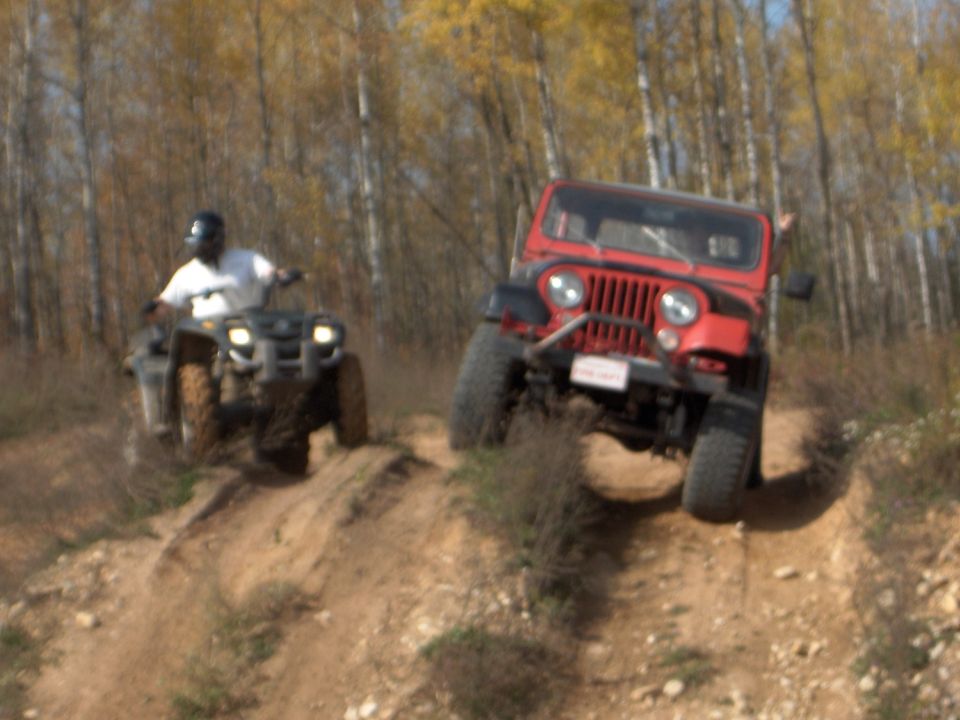 1979 Jeep CJ5 and ATV climbing a dirt hill, trees in background