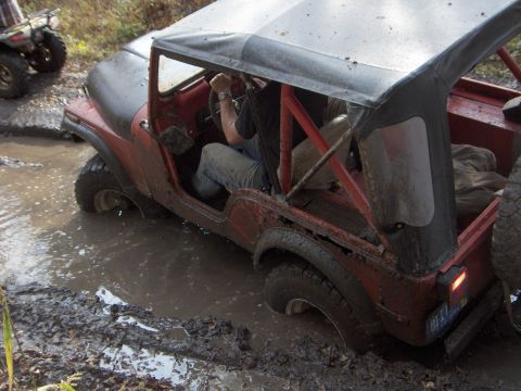 1979 Jeep CJ5 - A red Jeep CJ navigates a muddy obstacle during an off-road event, while another vehicle waits behind.