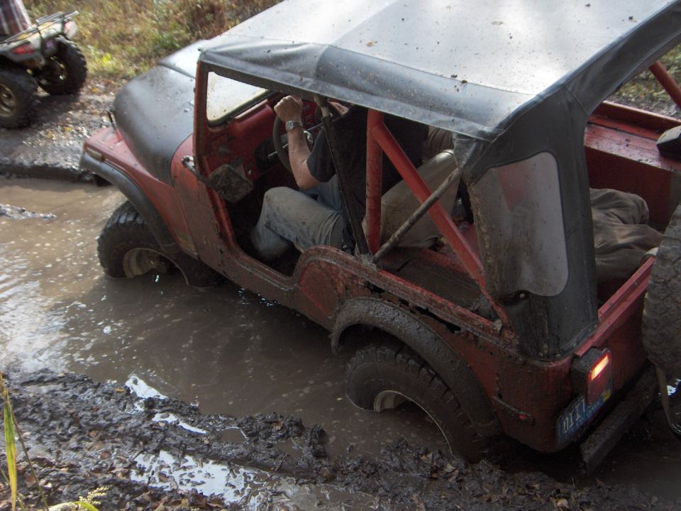 Red Jeep CJ stuck in mud, with an ATV in the background