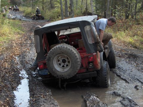 1979 Jeep CJ5 - A 1979 Jeep CJ5 is stuck in the mud during an off-road run, with assistance from passengers and other vehicles nearby.