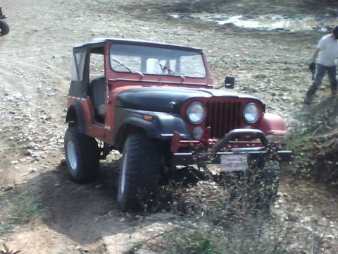 1979 Jeep CJ5 - Red 1979 Jeep CJ5 with a soft top navigates an off-road trail, displaying a 'FIRE DEPT' license plate.