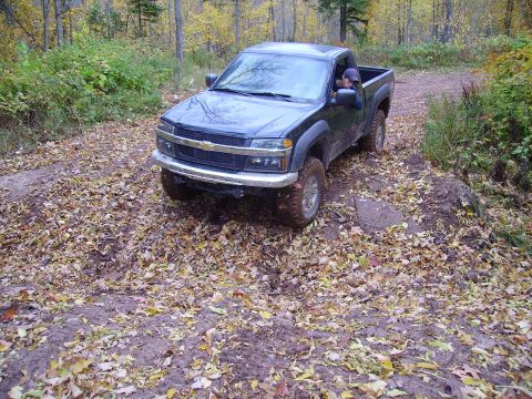 2000 Chevrolet Tahoe - A black pickup truck navigates a muddy, leaf-strewn path through an autumn forest.